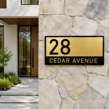 Custom black and gold acrylic house number and street name sign displaying 28 Cedar Avenue on a modern stone wall