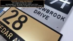 Close-up of black, gold and white layered acrylic house number signs shown as a colour and finish reference.